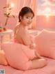 A woman sitting on a bed with pink pillows.