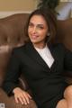 A woman in a black suit sitting on a brown couch.