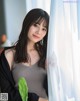 A woman leaning against a curtain with a plant in her hand.