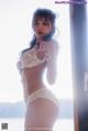 A woman in a white lingerie posing by a window.